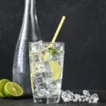 glass of water with sparkling water with lemon, lemon slices next to a glass bottle