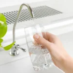 hand holding glass of water and filling from the tap with a green plant on the left