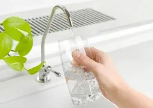 hand holding glass of water and filling from the tap with a green plant on the left